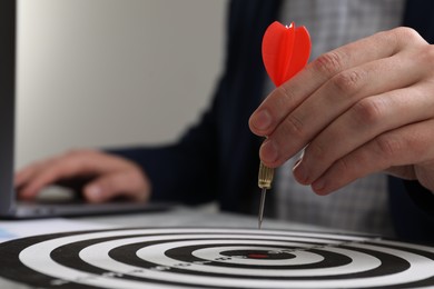 Business targeting concept. Man with dart aiming at dartboard at table, closeup