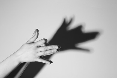 Photo of Shadow puppet. Woman making hand gesture like dog on light background, closeup. Black and white effect