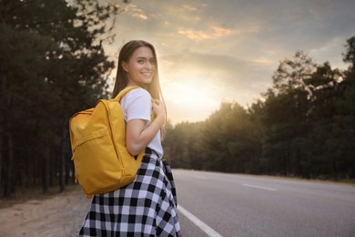 Happy young woman with backpack on road near forest