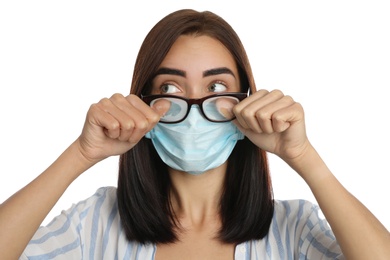 Photo of Young woman wiping foggy glasses caused by wearing disposable mask on white background. Protective measure during coronavirus pandemic