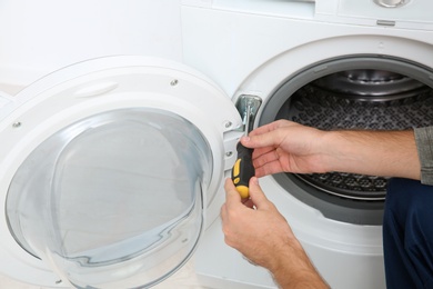 Young plumber fixing washing machine in bathroom