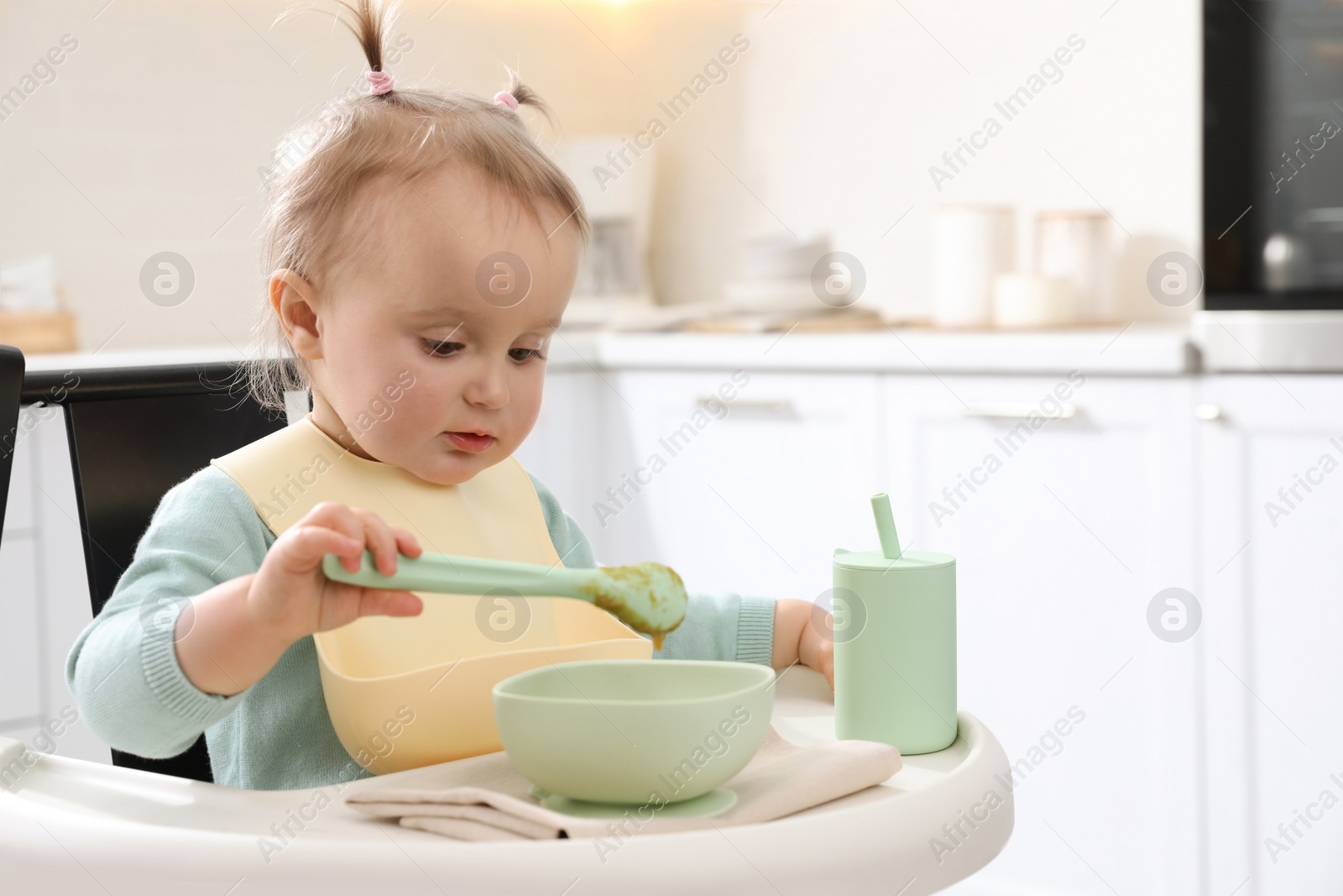 Photo of Cute little baby eating food in high chair at kitchen