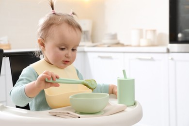 Cute little baby eating food in high chair at kitchen