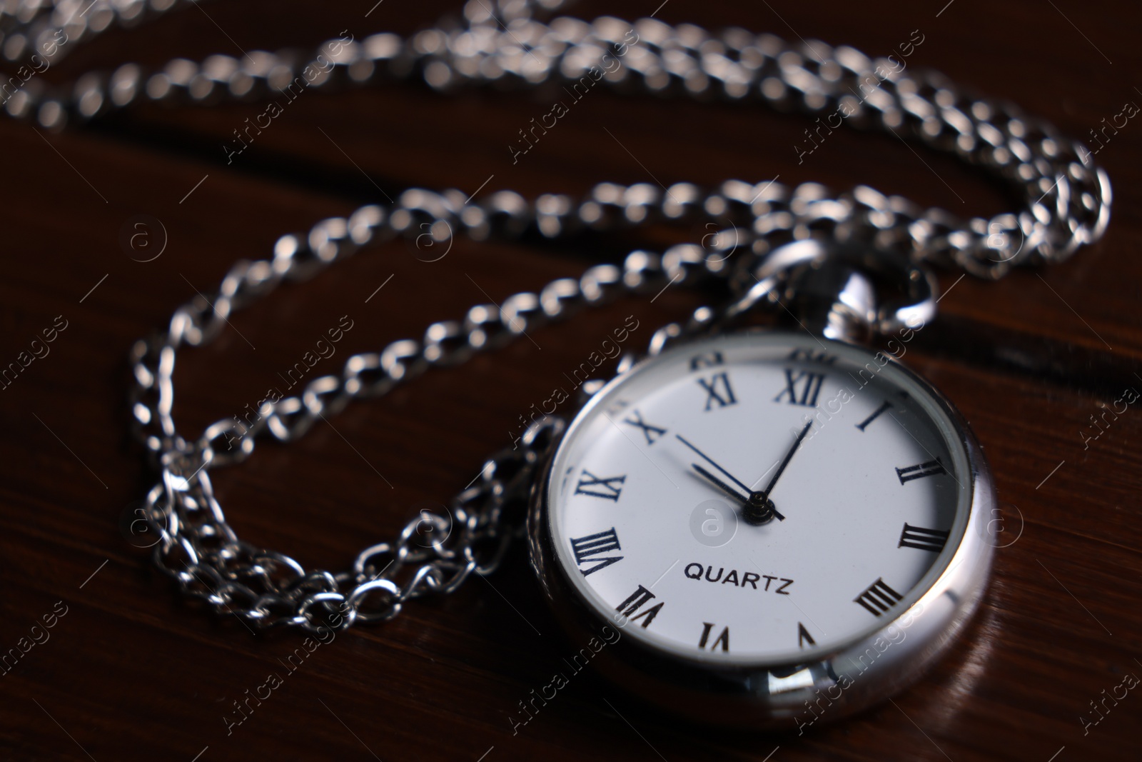 Photo of Silver pocket clock with chain on wooden table, closeup