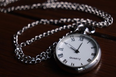 Photo of Silver pocket clock with chain on wooden table, closeup