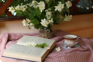 Photo of Beautiful jasmine flowers, cup of aromatic drink and open book on pink fabric indoors