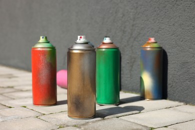 Cans of different spray paints on pavement near wall