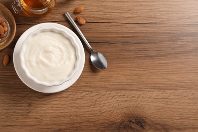 Photo of Bowl with delicious semolina pudding near honey and almonds on wooden table, flat lay. Space for text