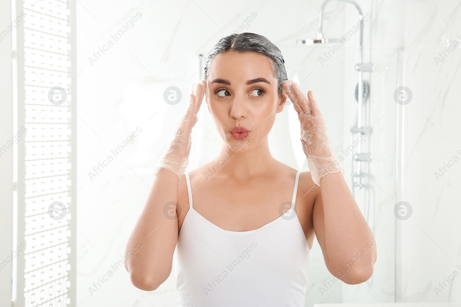 Photo of Young woman dyeing her hair in bathroom