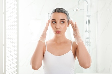 Photo of Young woman dyeing her hair in bathroom