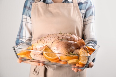 Woman holding raw chicken with orange slices on light grey background, closeup