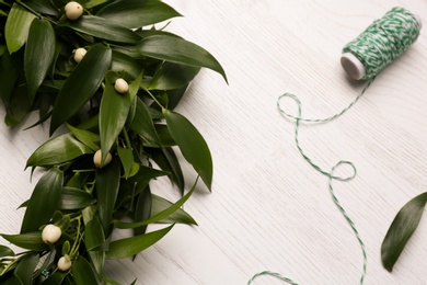 Photo of Beautiful handmade mistletoe wreath and thread spool on white wooden table. Traditional Christmas decor