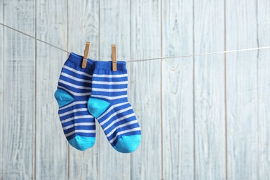 Photo of Pair of socks on laundry line against wooden background, space for text. Baby accessories