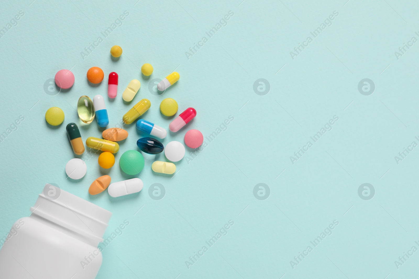 Photo of Plastic bottle with many different pills on light blue background, flat lay. Space for text