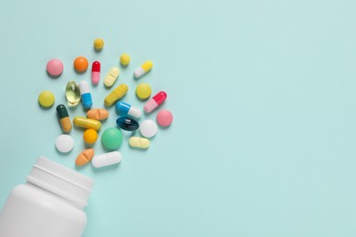 Photo of Plastic bottle with many different pills on light blue background, flat lay. Space for text