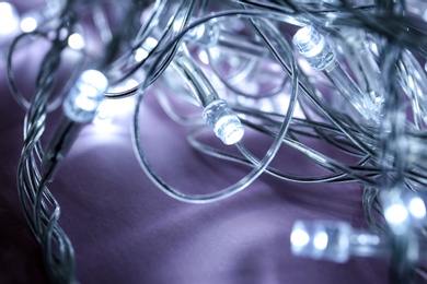 Photo of Glowing Christmas lights on violet background, closeup