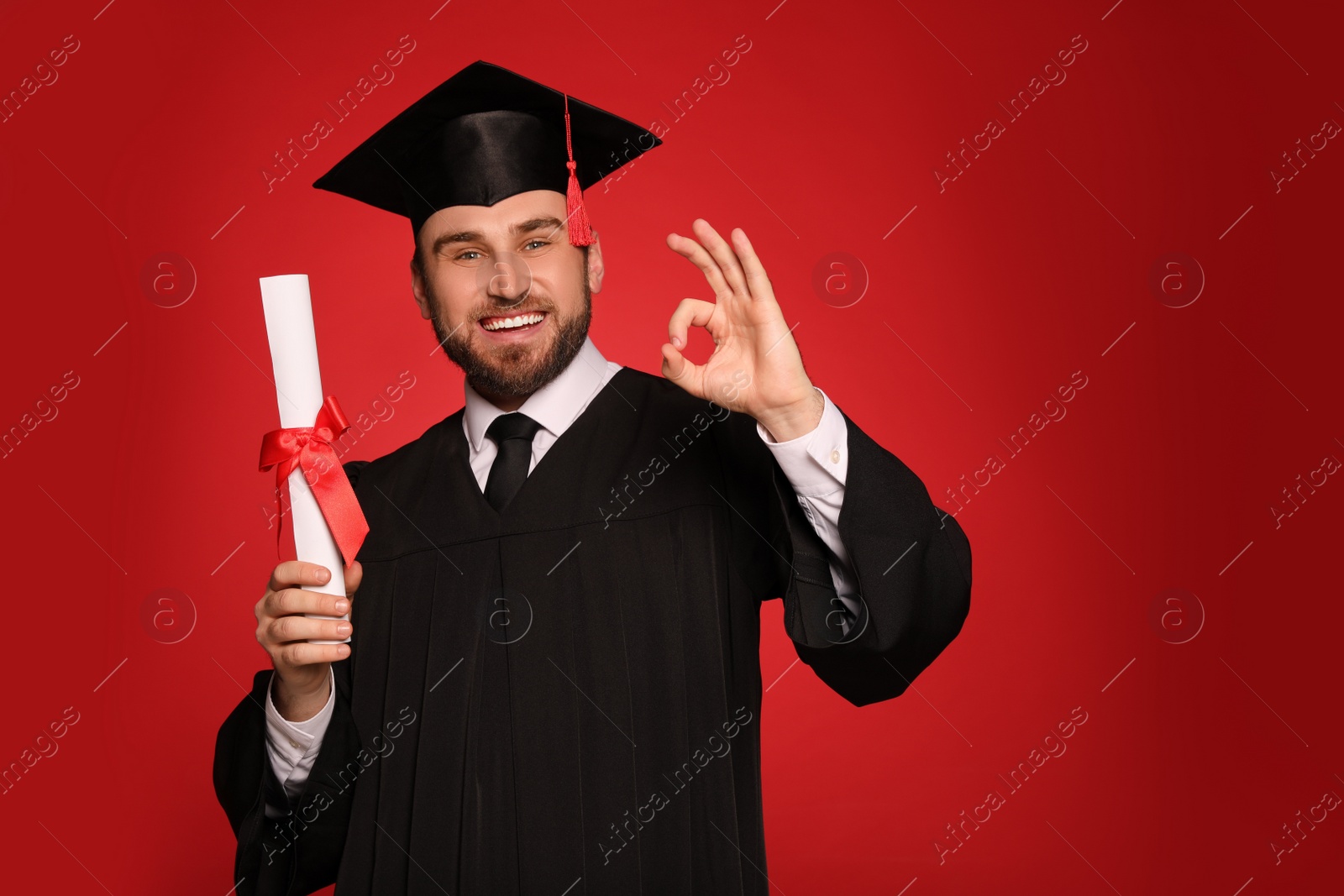 Photo of Happy student with graduation hat and diploma on red background