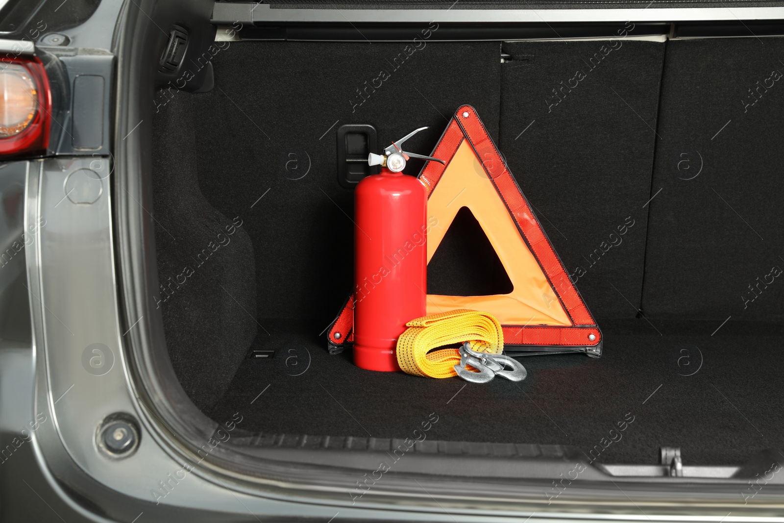 Photo of Red fire extinguisher, towing strap and foldable emergency warning triangle in trunk. Car safety