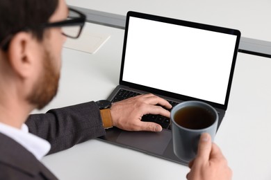 Photo of Man with cup of coffee working on laptop at white desk in office, closeup