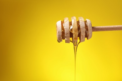 Delicious honey flowing down from dipper against yellow background. Space for text