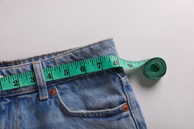 Photo of Jeans with measuring tape on light grey background, top view. Weight loss concept