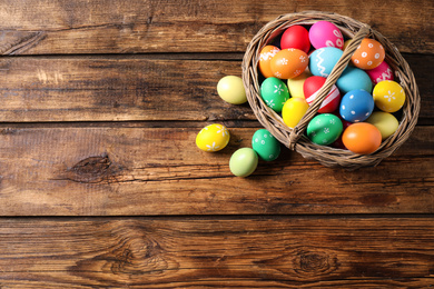 Photo of Colorful Easter eggs in basket on wooden background, flat lay. Space for text