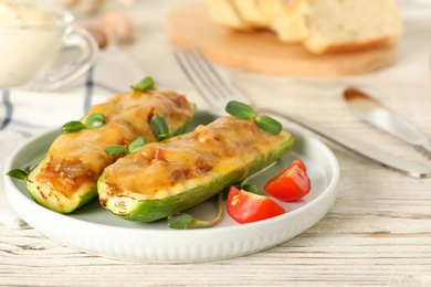 Photo of Baked stuffed zucchinis served with tomatoes on white wooden table, closeup