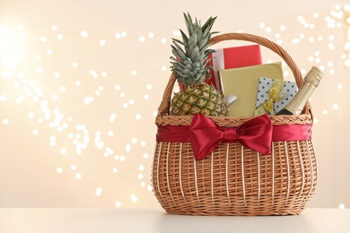 Photo of Wicker basket with gifts, champagne and food against blurred festive lights. Space for text