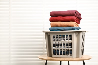 Plastic laundry basket with clean clothes on wooden table indoors. Space for text