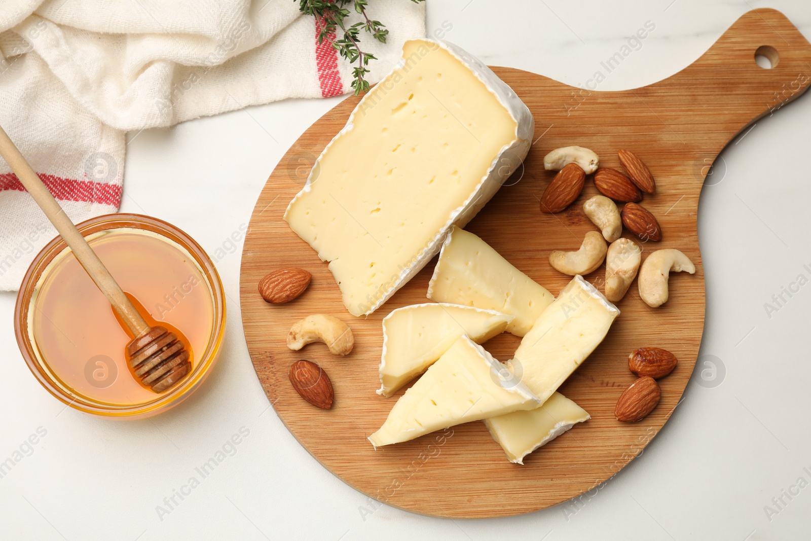 Photo of Tasty Camembert cheese with honey and nuts on white table, flat lay