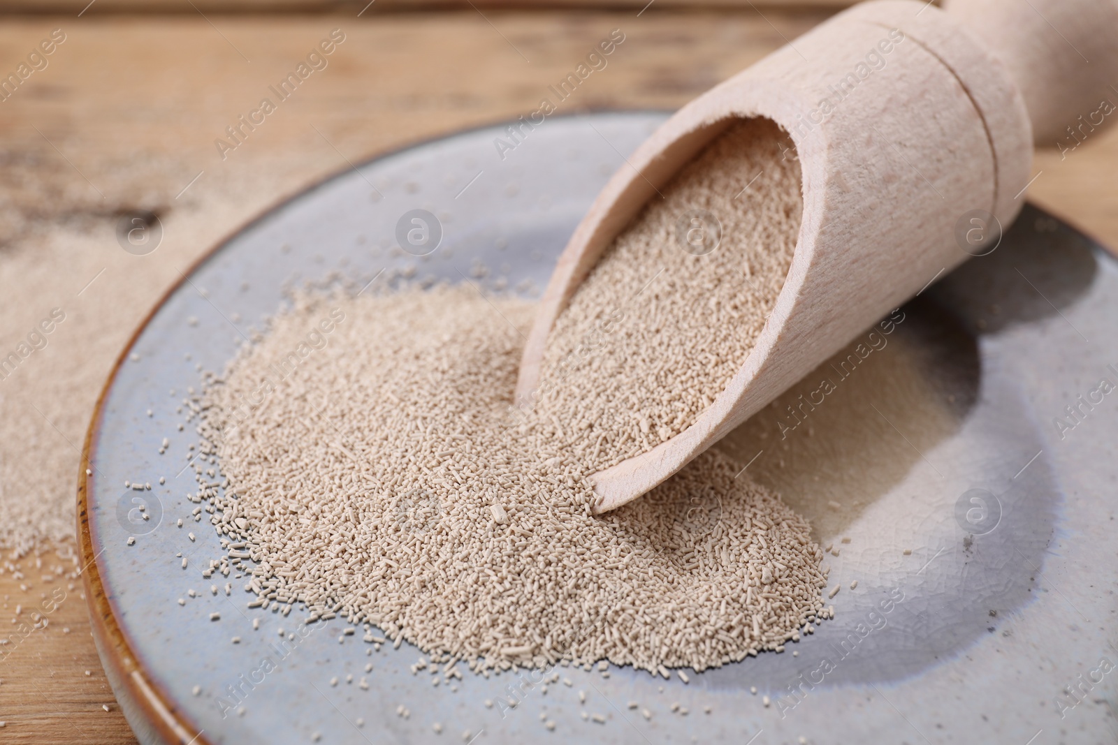 Photo of Plate and scoop with active dry yeast on wooden table, closeup