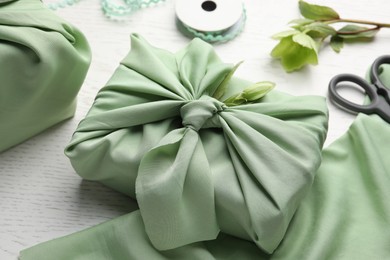 Furoshiki technique. Gift packed in green fabric and decorated with hellebore flower on white wooden table, closeup