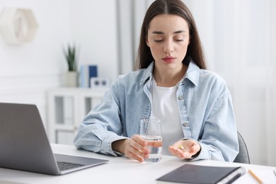 Photo of Woman with pill and glass of water suffering from headache at workplace in office