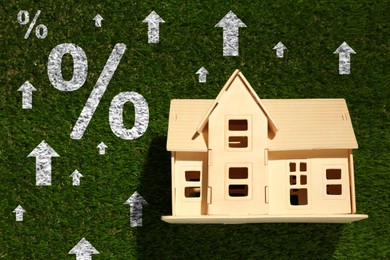 Image of Mortgage rate rising illustrated by upward arrows and percent signs. House model on green grass, top view