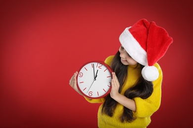 Photo of Girl in Santa hat with clock on red background, space for text. New Year countdown