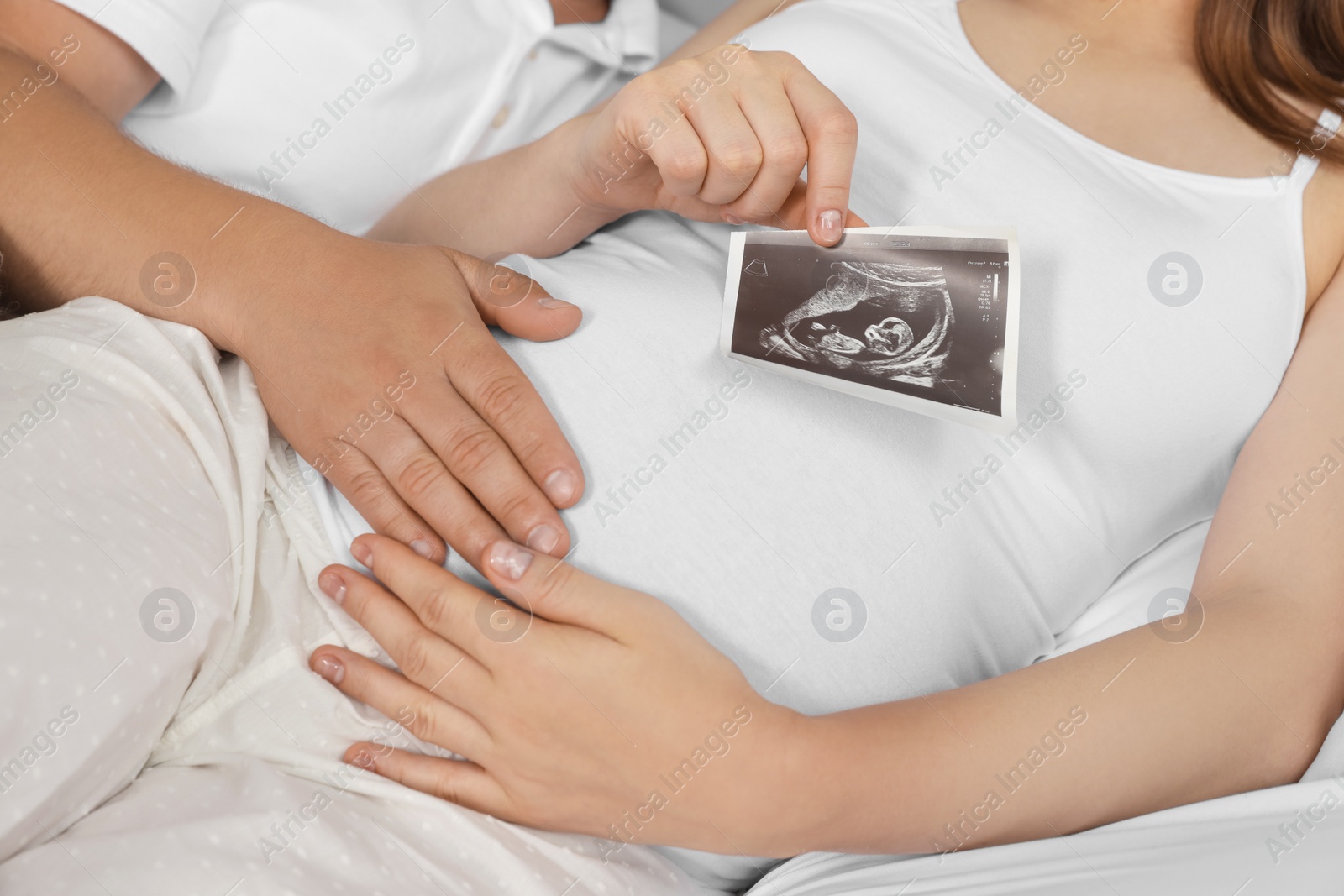 Photo of Man hugging his pregnant wife with ultrasound scan on bed, closeup