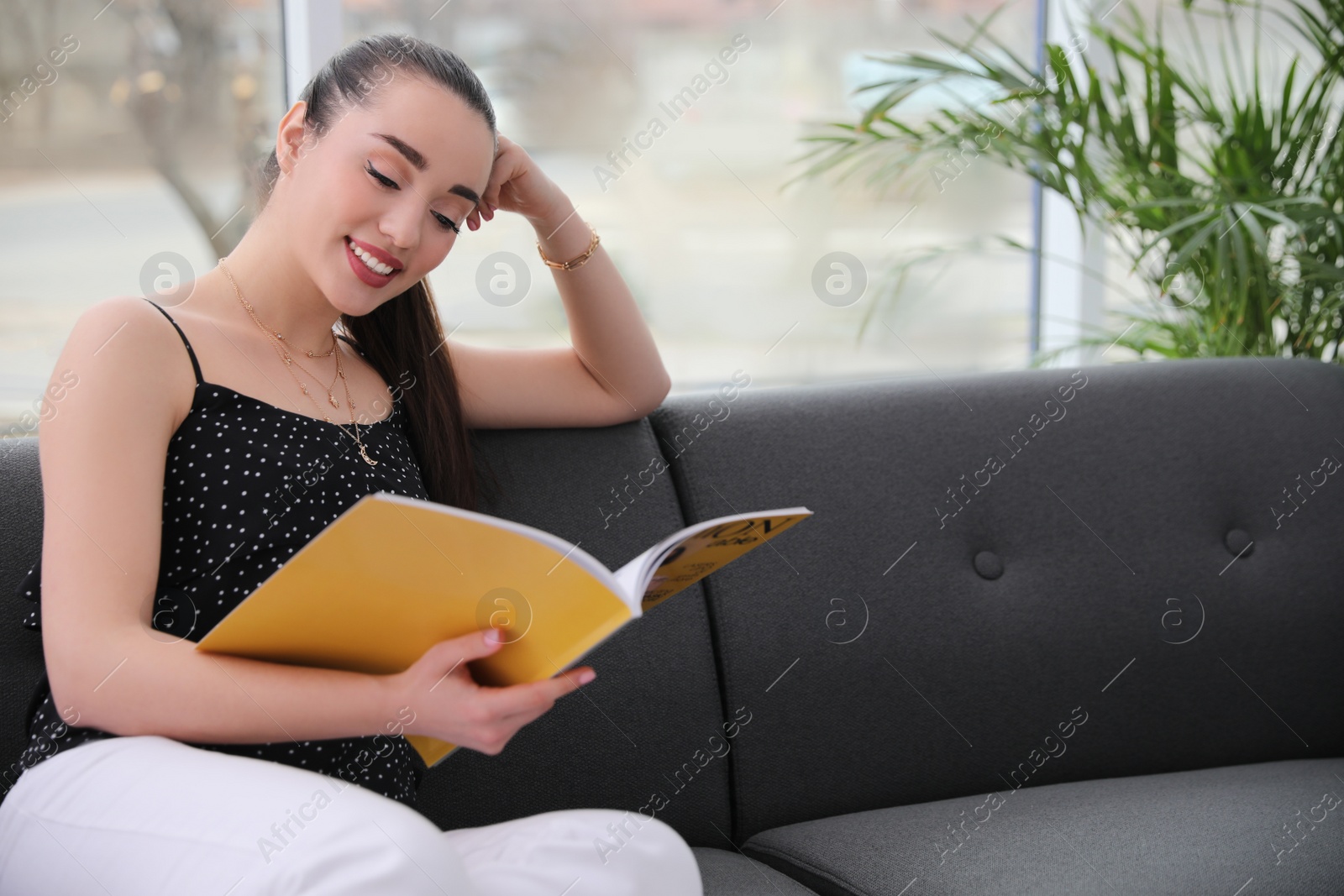 Photo of Happy woman reading magazine on sofa at home