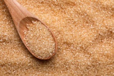 Photo of Brown granulated sugar and wooden spoon as background, closeup