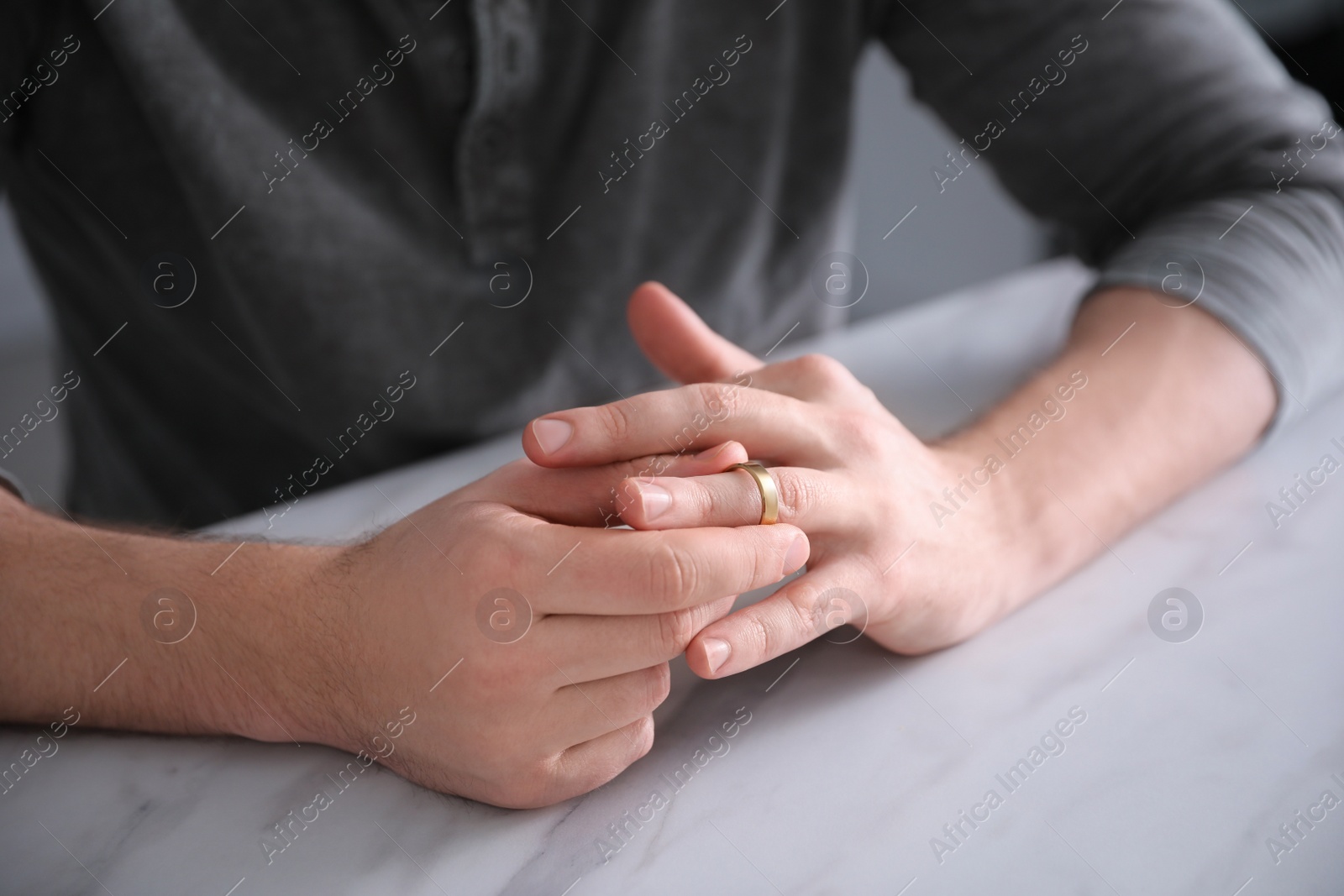 Photo of Man taking off wedding ring at white marble table, closeup. Divorce concept