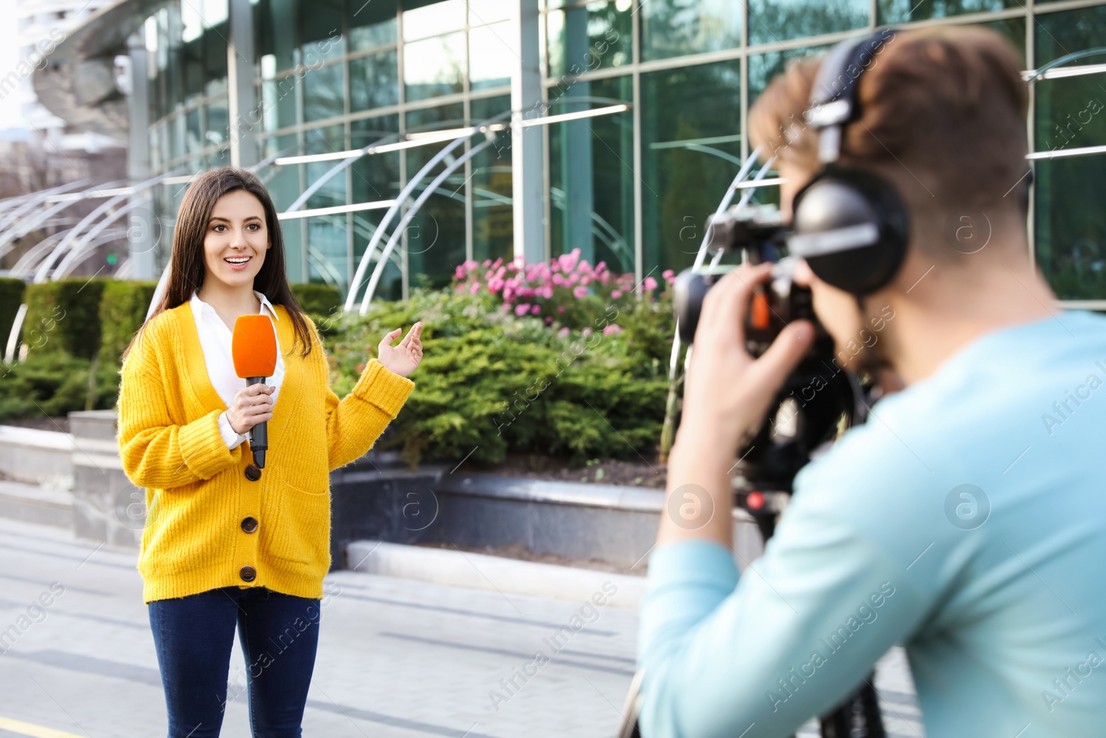 Photo of Young journalist and video operator working on city street