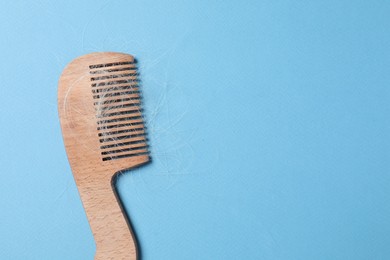 Photo of Wooden comb with lost hair on light blue background, top view. Space for text