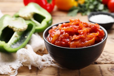 Photo of Bowl of delicious lecho and ingredients on wooden table, closeup