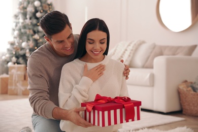 Photo of Boyfriend giving Christmas gift box to his girlfriend in living room