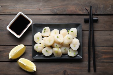 Photo of Raw scallops with green onion, soy sauce, lemon and chopsticks on wooden table, flat lay