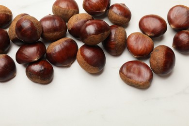 Photo of Sweet fresh edible chestnuts on white marble table, top view. Space for text