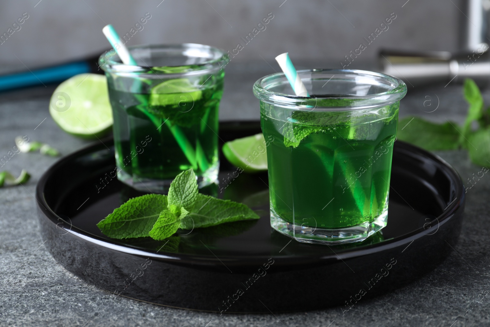 Photo of Delicious mint liqueur with green leaves and lime on grey table