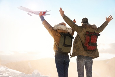 Excited couple in mountains under sky with flying airplane. Winter vacation