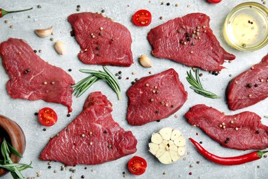 Photo of Fresh raw meat steaks and spices on light grey table, flat lay