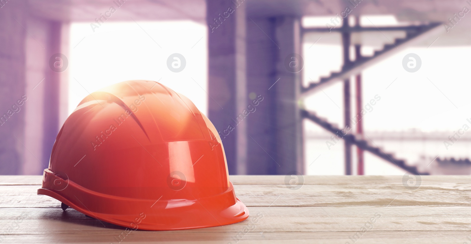 Image of Hard hat on wooden surface at construction site with unfinished building. Space for text 