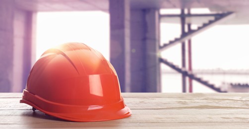 Image of Hard hat on wooden surface at construction site with unfinished building. Space for text 